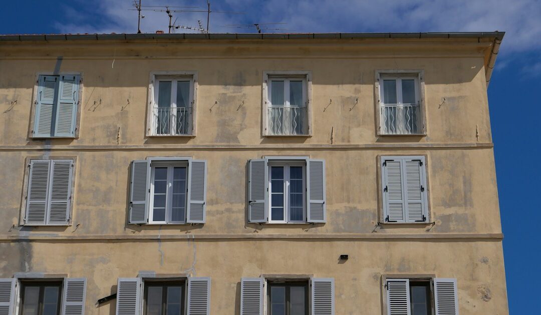 Façade d'immeuble ocre aux volets gris sous un ciel bleu