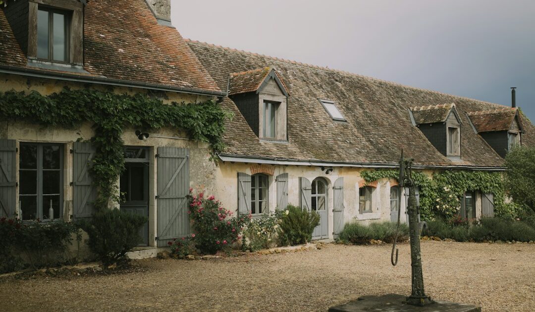Longère en pierre aux volets gris et sa cour en gravier, dans la campagne française